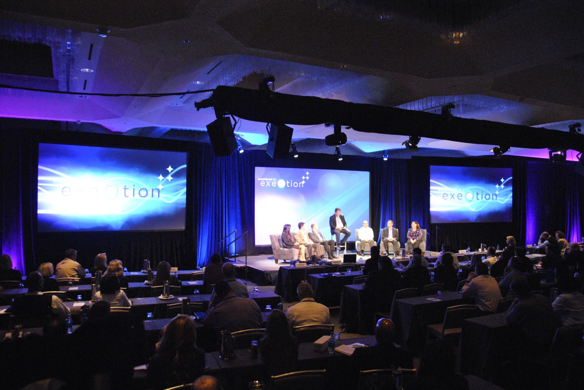 Panel session on a lit stage with LED screens and truss-mounted lighting